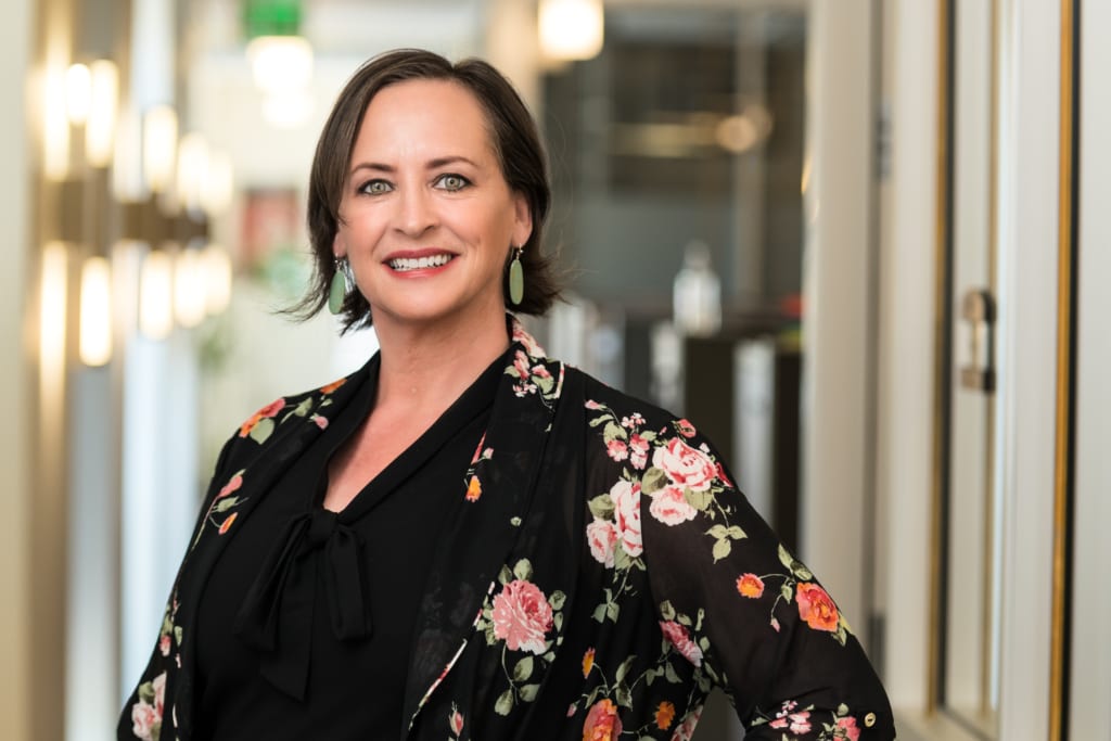 Carrie Christoper of Newmont stands in a floral jacket facing the camera.