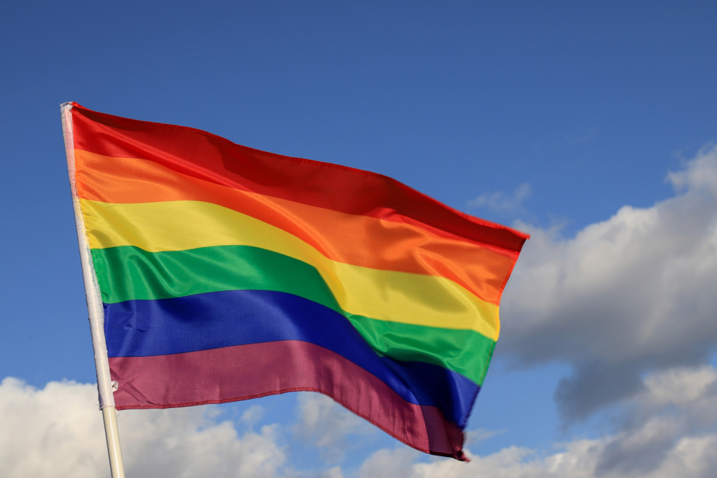 A rainbow Pride flag waves in front of a blue sky.