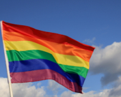 A rainbow Pride flag waves in front of a blue sky.
