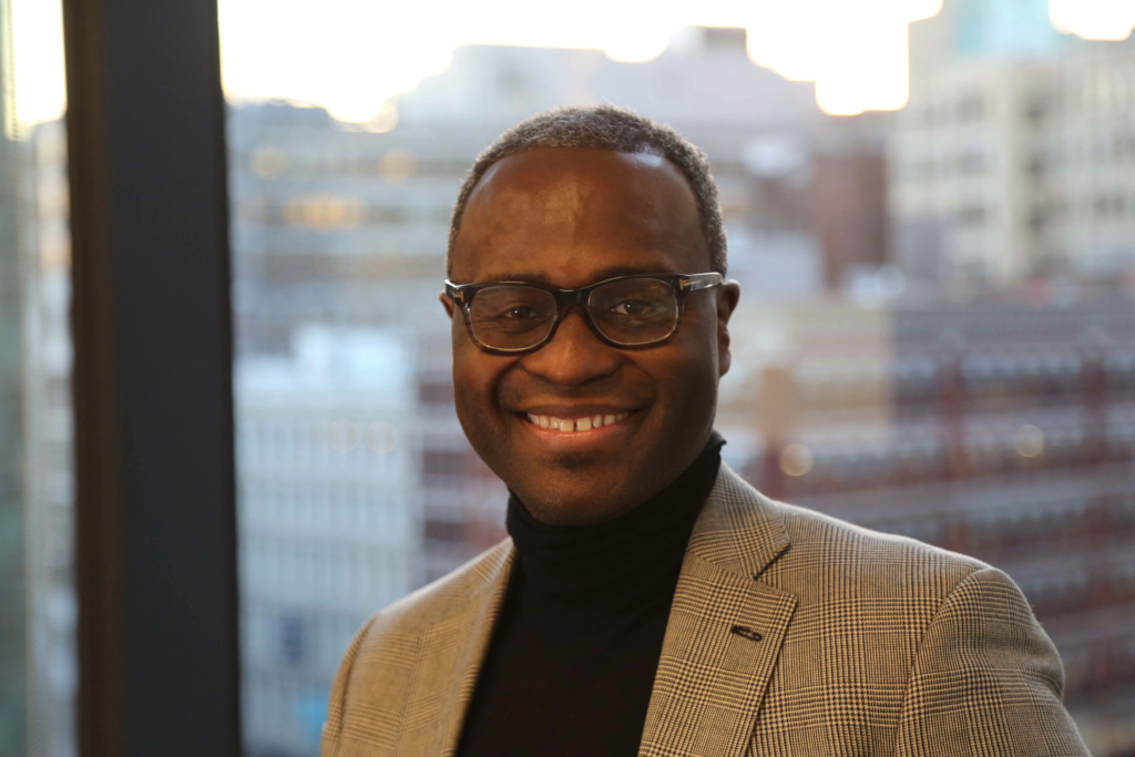 Obed Louissaint, SVP, Transformation and Culture at IBM, looks to camera wearing a snazzy tan jacket.